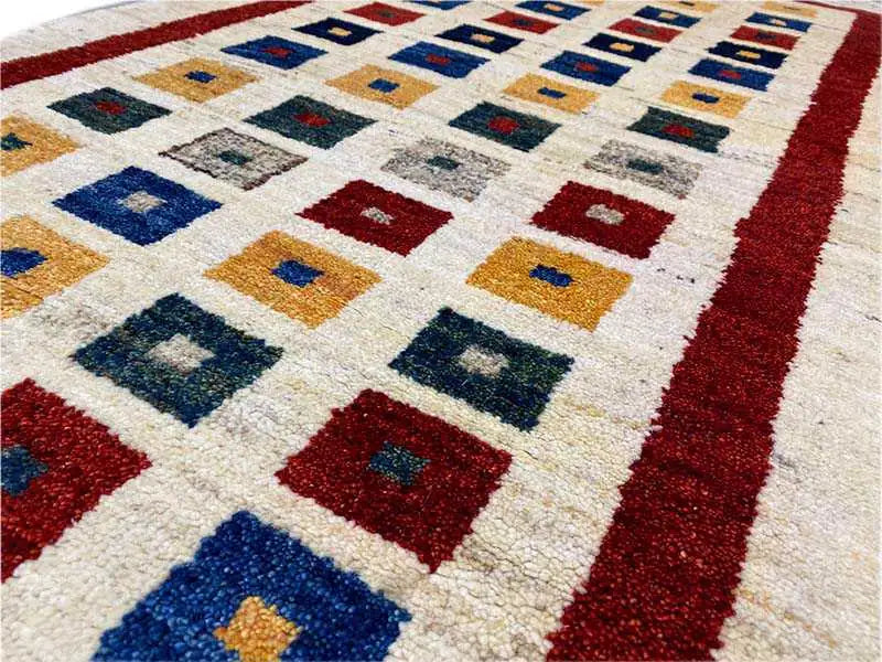 Close-up of a Gabbeh rug: geometric squares in blue, red, and yellow on cream