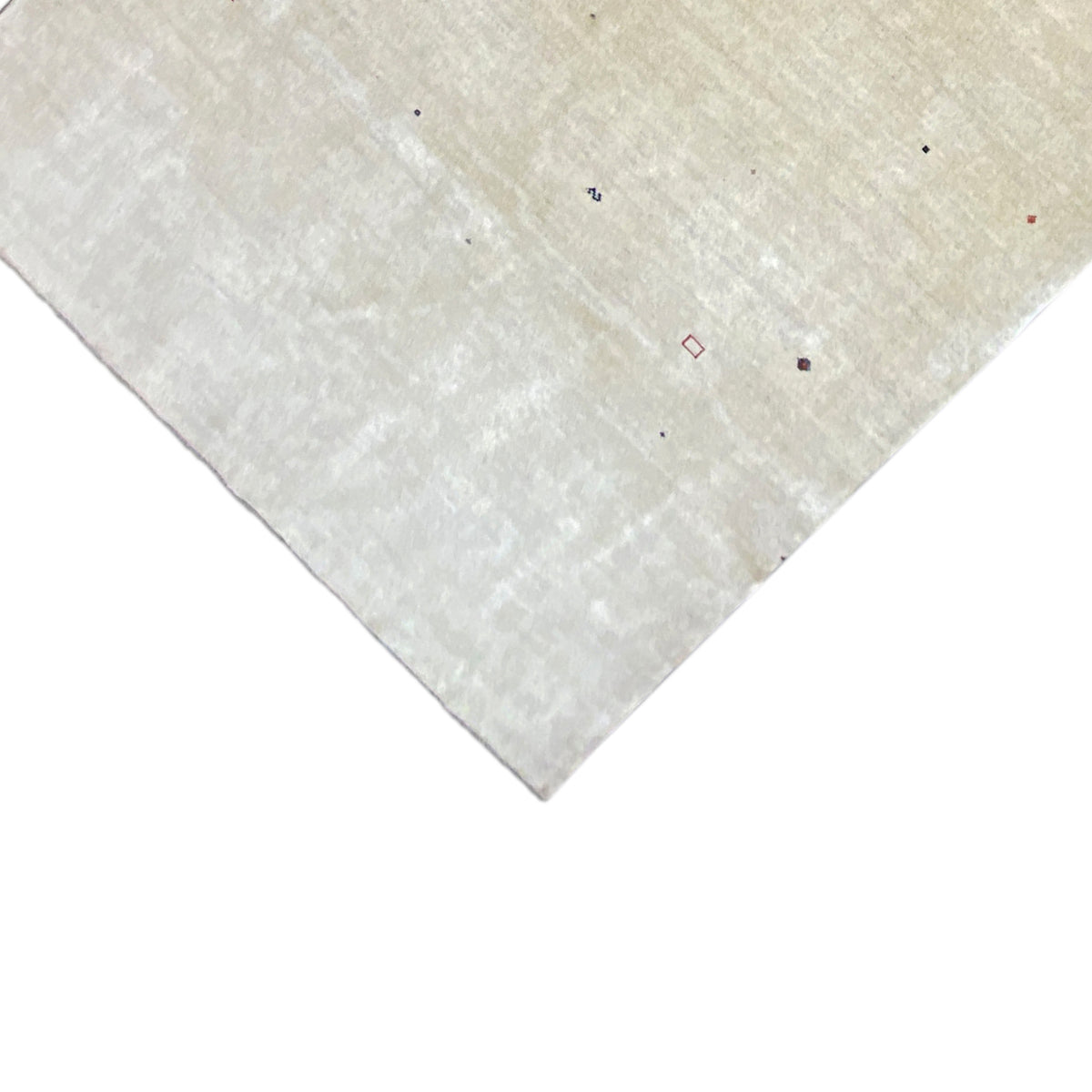 Corner of a beige Gabbeh rug with colorful dots and a short pile edge.