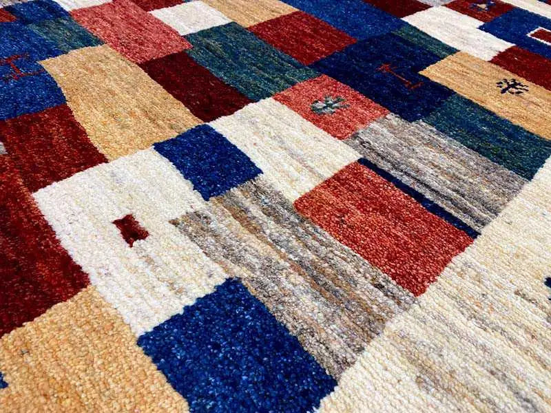 Gabbeh rug pattern detail: red, blue, and beige squares with mottled fiber transitions.