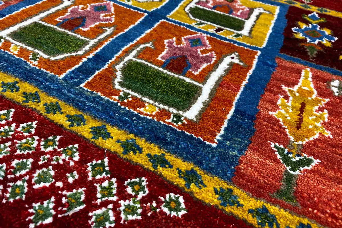 Close-up: Gabbeh rug with red pile, blue border, and green and gold house motifs