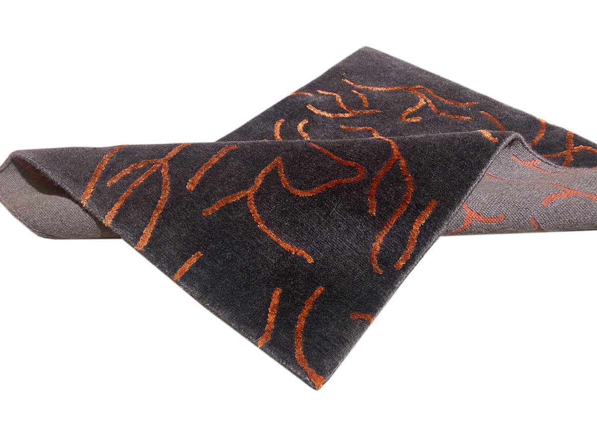 Designer rug in dark gray with an orange abstract pattern, shown folded-looking