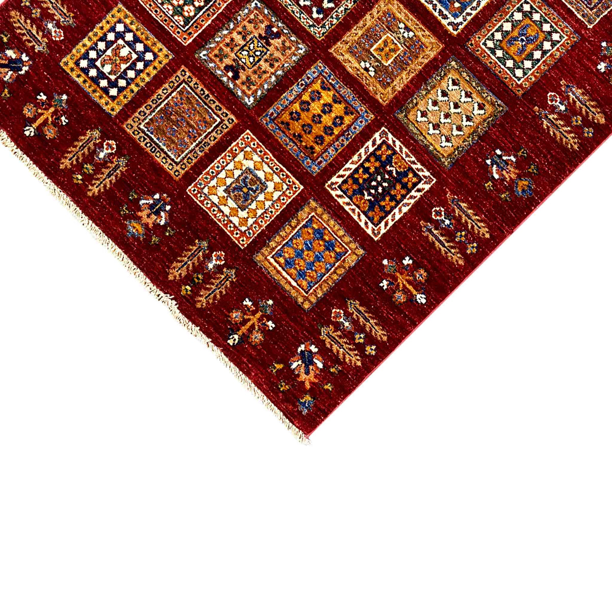 Close-up of the corner: deep red Khorjin wool rug with colorful tile motifs and fringe.
