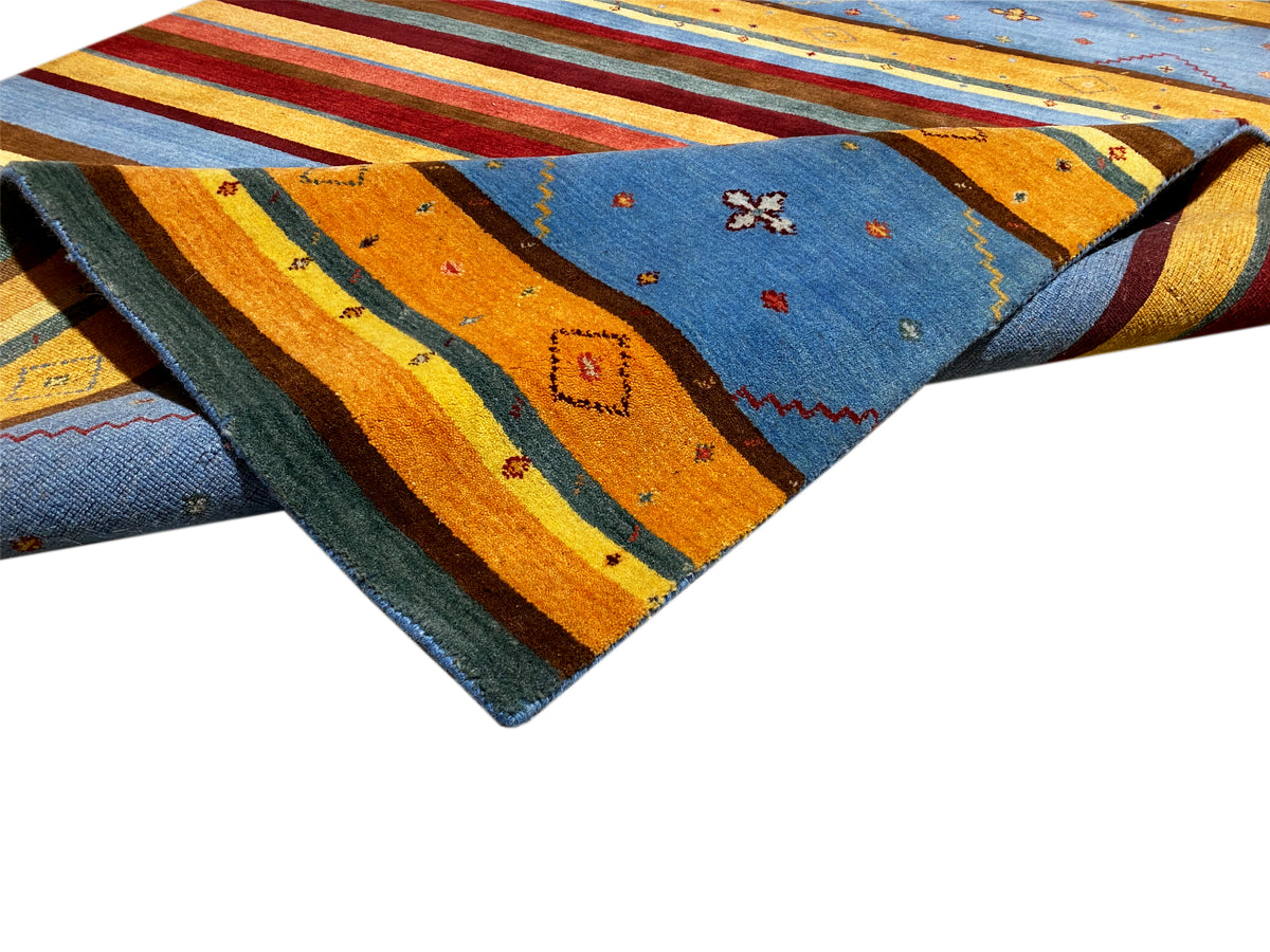 Loom Luri Teppich leicht überlappend: Streifen in Blau, Gelb, Orange und dunklem Grün.