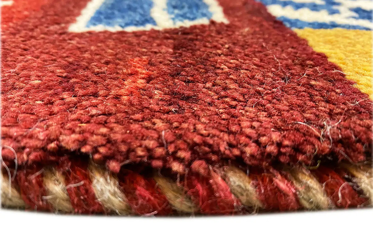 Gabbeh rug detail: red pile texture with a blue pattern and a crimped fringed edge