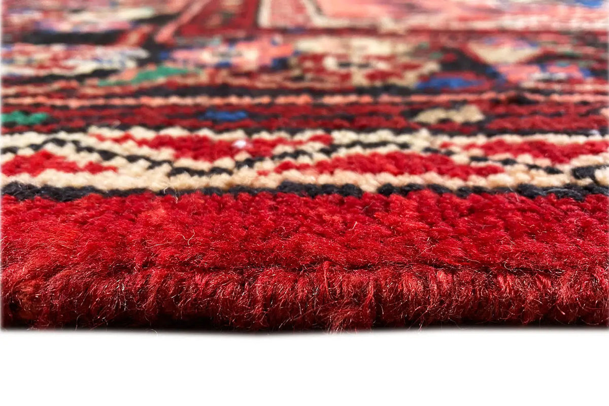 Carpet pile in close-up: dense red pile with multicolored decorative bands along the edge