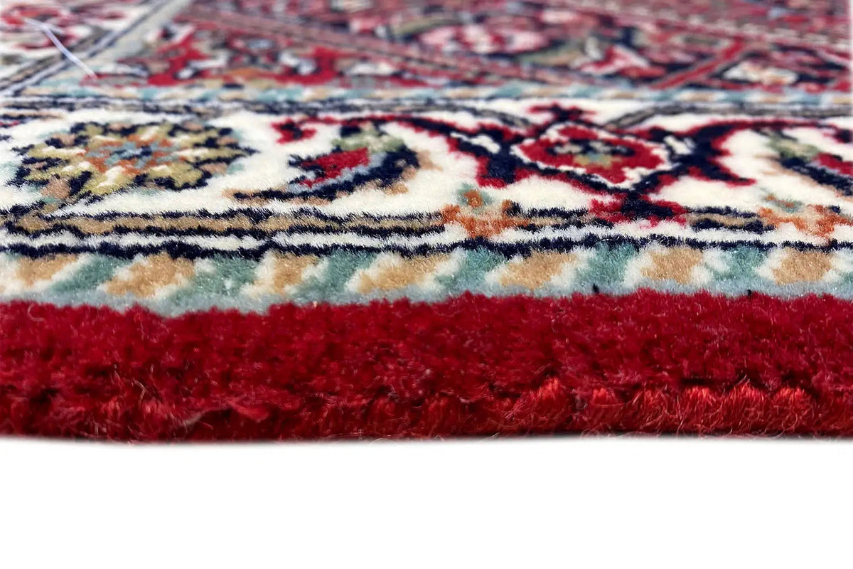 Rug edge with fringe and red pile, above it a multicolored ornamental pattern