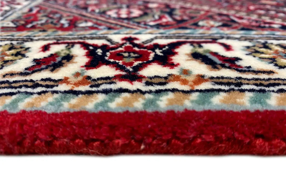 Close-up of carpet edge: red pile, multicolored patterned border, and short fringes