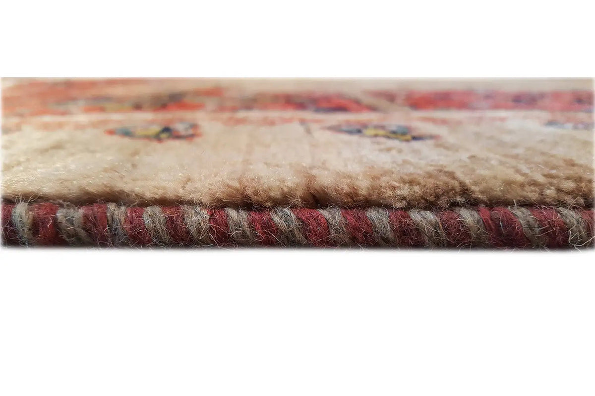 Oriental rug edge with beige pile, a multicolored red border, and fringed end threads