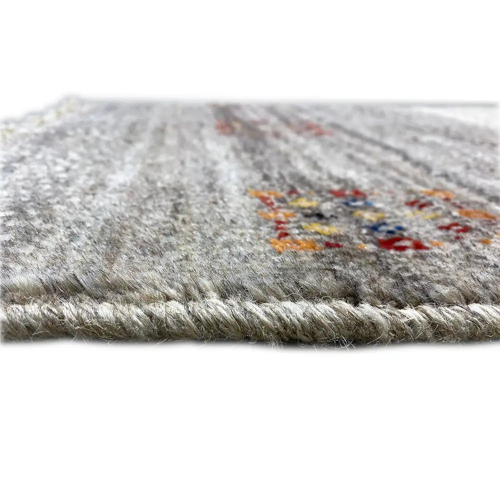 Gabbeh rug close-up at the edge: gray woven texture, colorful embroidered motifs, fringe
