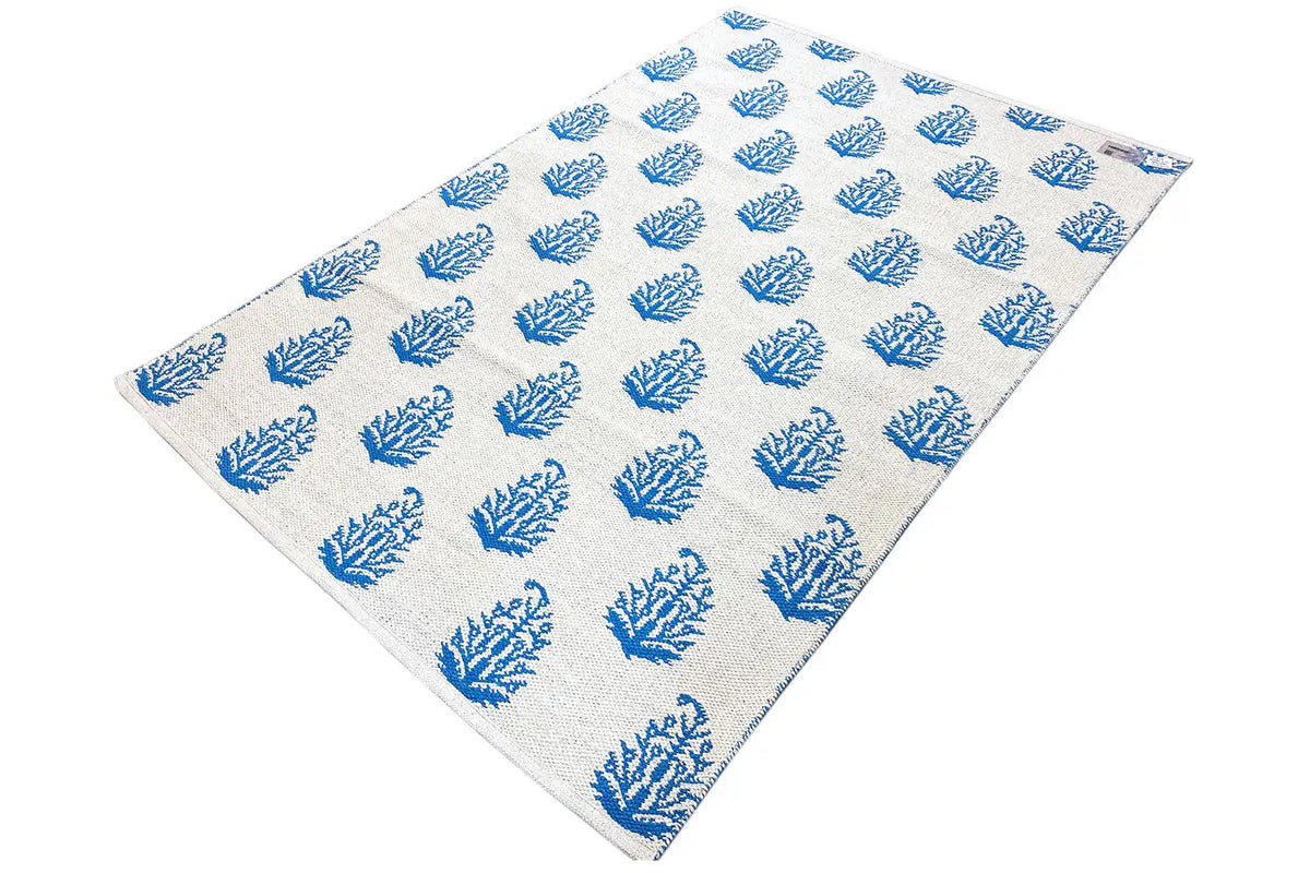 Cream-colored kilim with blue tree/branch motifs, compact weave structure and edges.