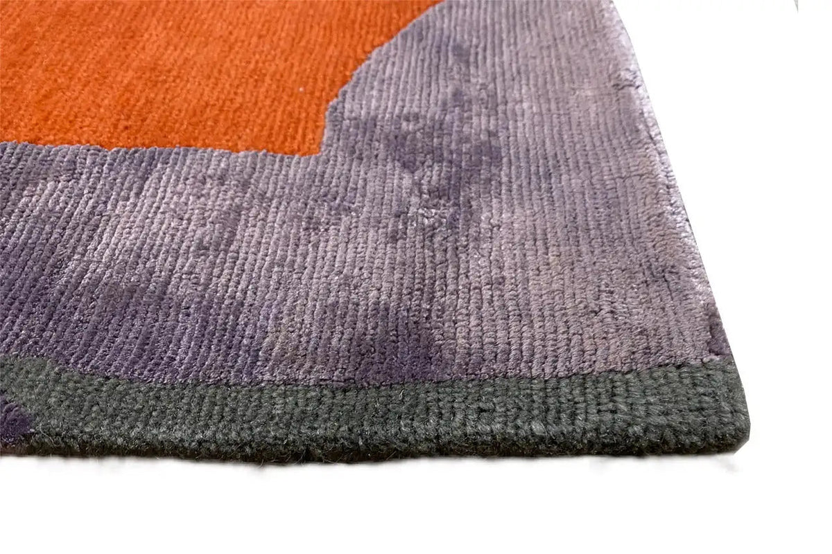 Close-up of designer rug: textured pile, purple surface with an orange corner