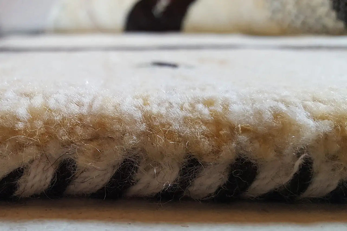 Detail of the carpet edge: dense pile with black-and-beige color distribution and a fine texture