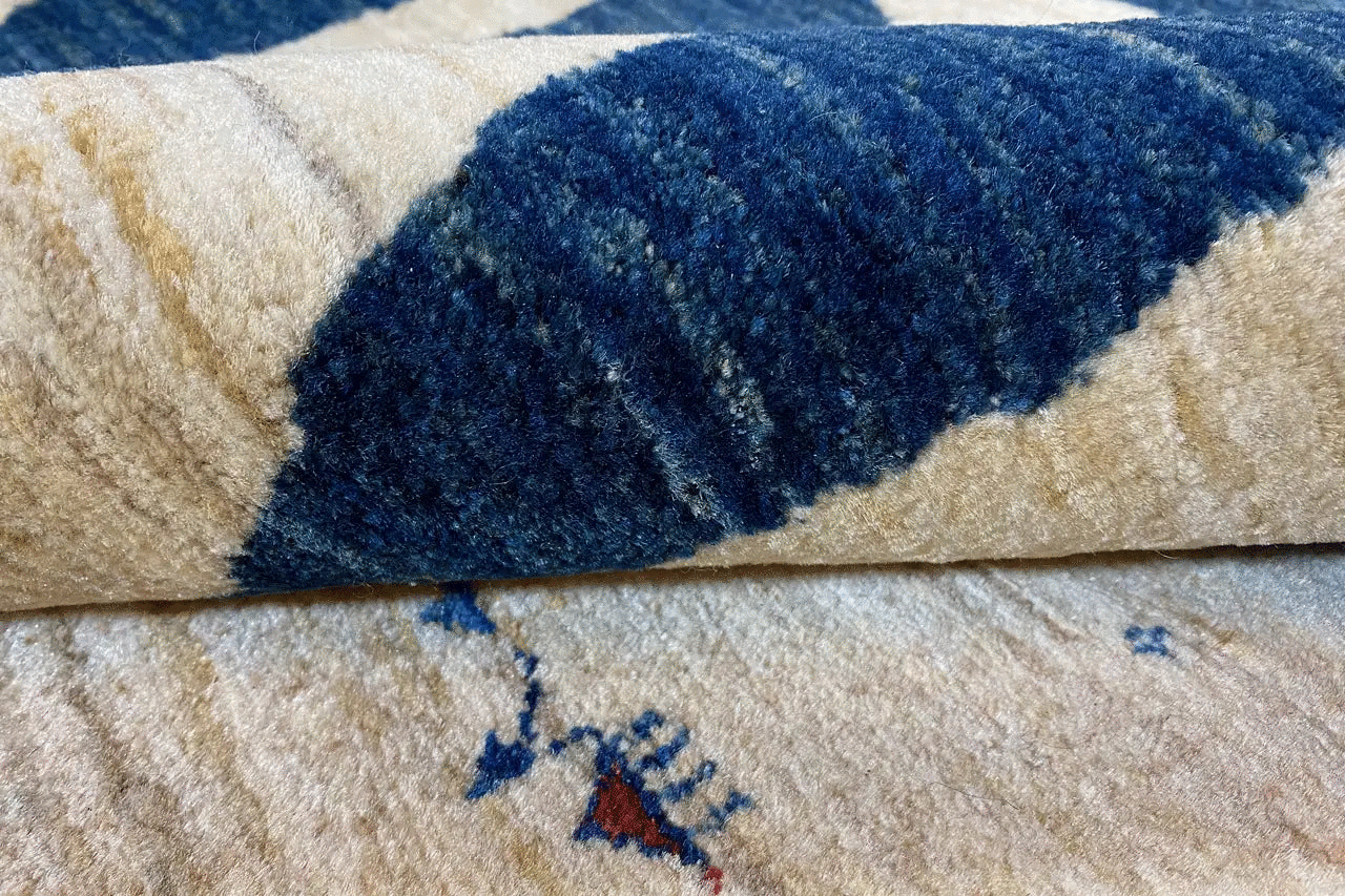 Close-up of a Gabbeh rug: beige pile with a blue pattern and woven seam