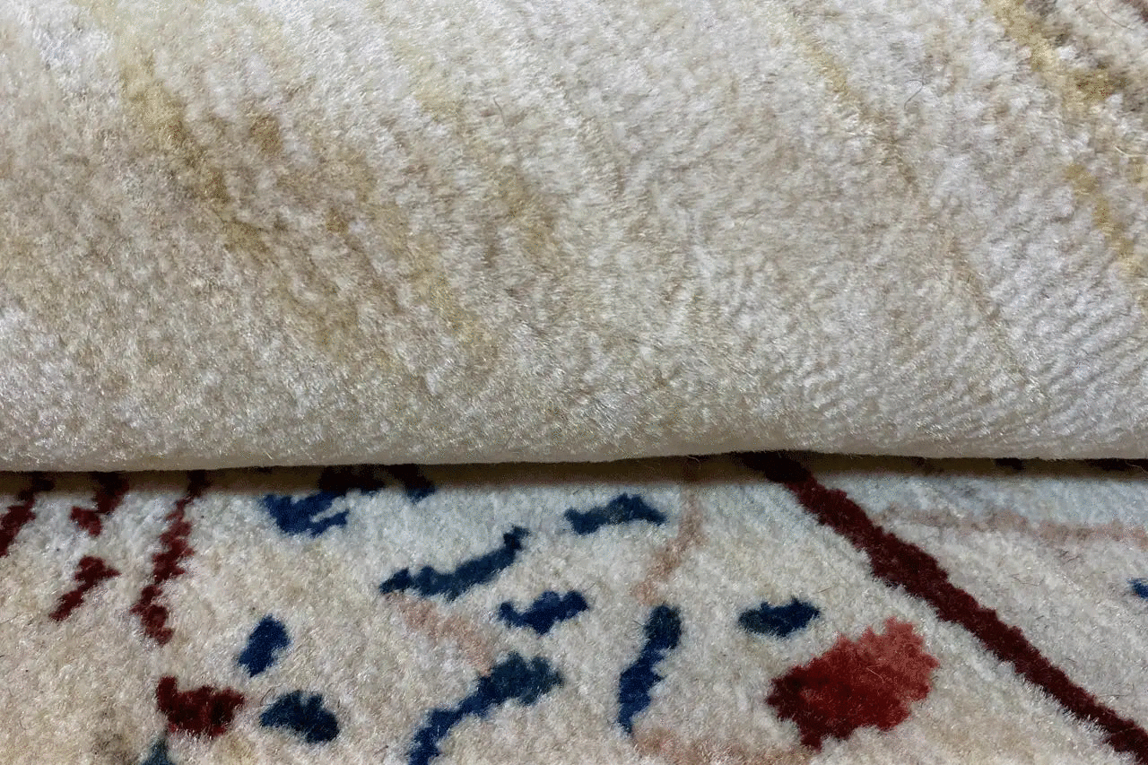 Wool rug pile in beige, detail with a pattern fragment underneath