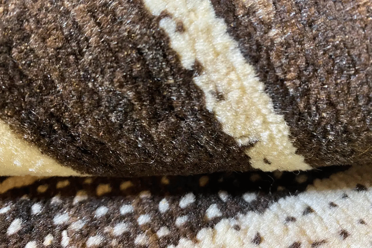 Close-up of carpet pile with a mottled brown, cream, and beige woven pattern.