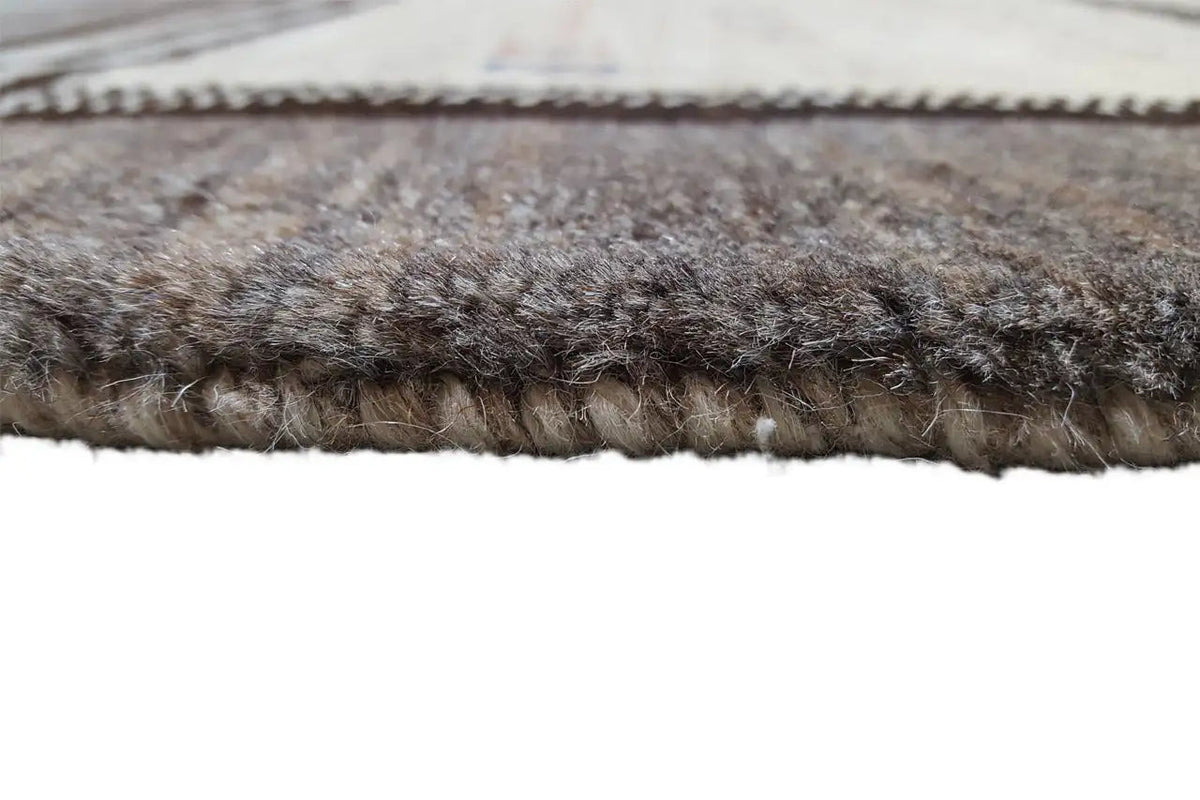 Close-up of a carpet edge: dense, dark brown pile with an even stitched edge