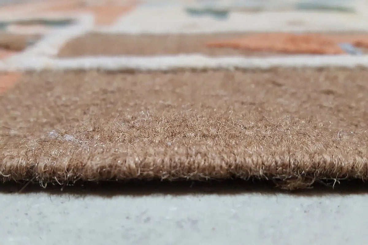 Close-up of the carpet edge with dense pile and a rough, brown woven texture