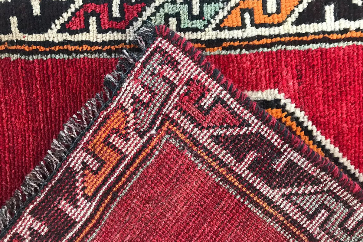 Close-up: red carpet with a multicolored patterned border and crossed textures