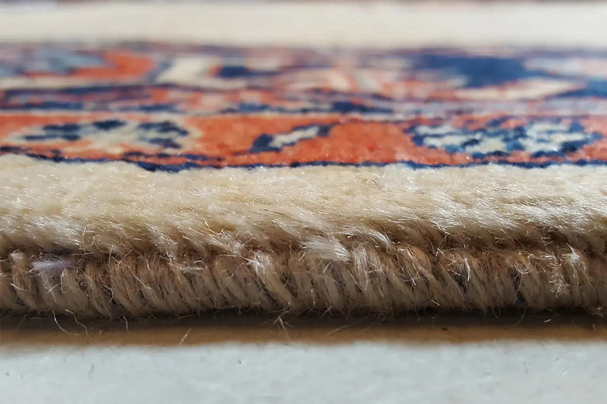 Carpet edge with short pile and frayed fibers on a blue-and-red patterned border
