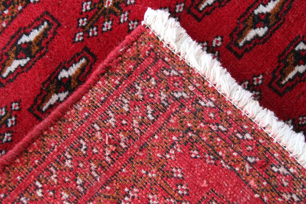 Turkmen carpet detail: red surface with a fine woven texture, diagonal pattern, and fringes