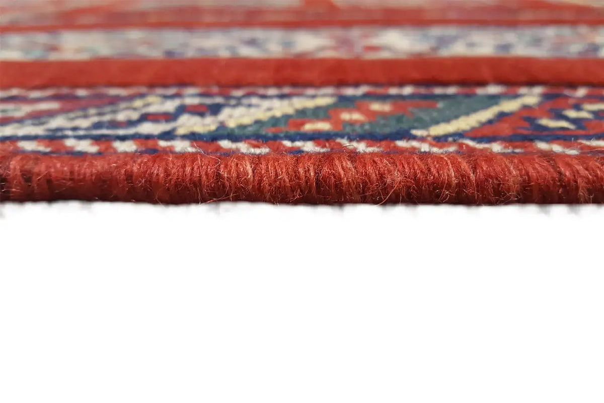 Edge detail of an Oriental rug with a red pile and delicate fringes