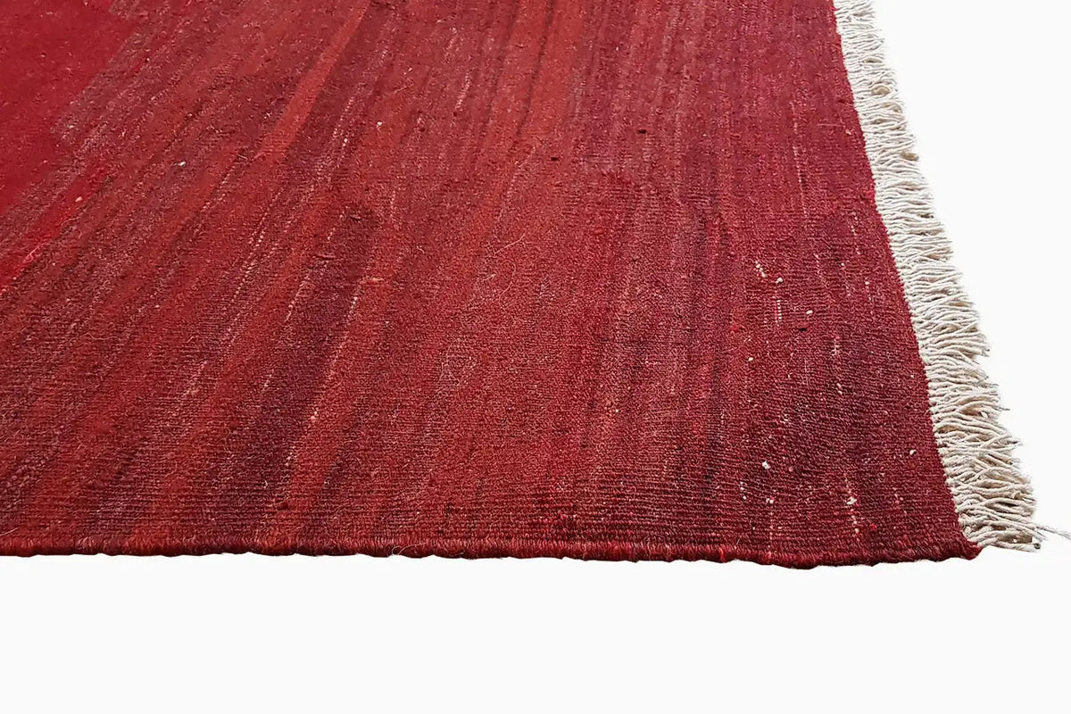 Red kilim rug with an irregular weave pattern and white fringe along the short side