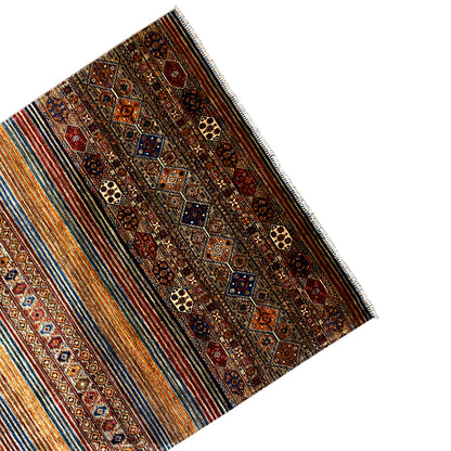 Khorjin rug viewed from the side, with borders and multicolored stripes, fringes along the edge.