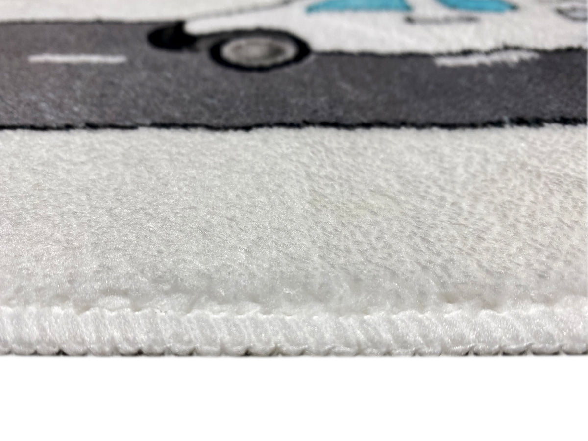 Kinderteppich-Detail am Rand: grauer Flor mit leichtem Stapel und farbigem Muster im Hintergrund.