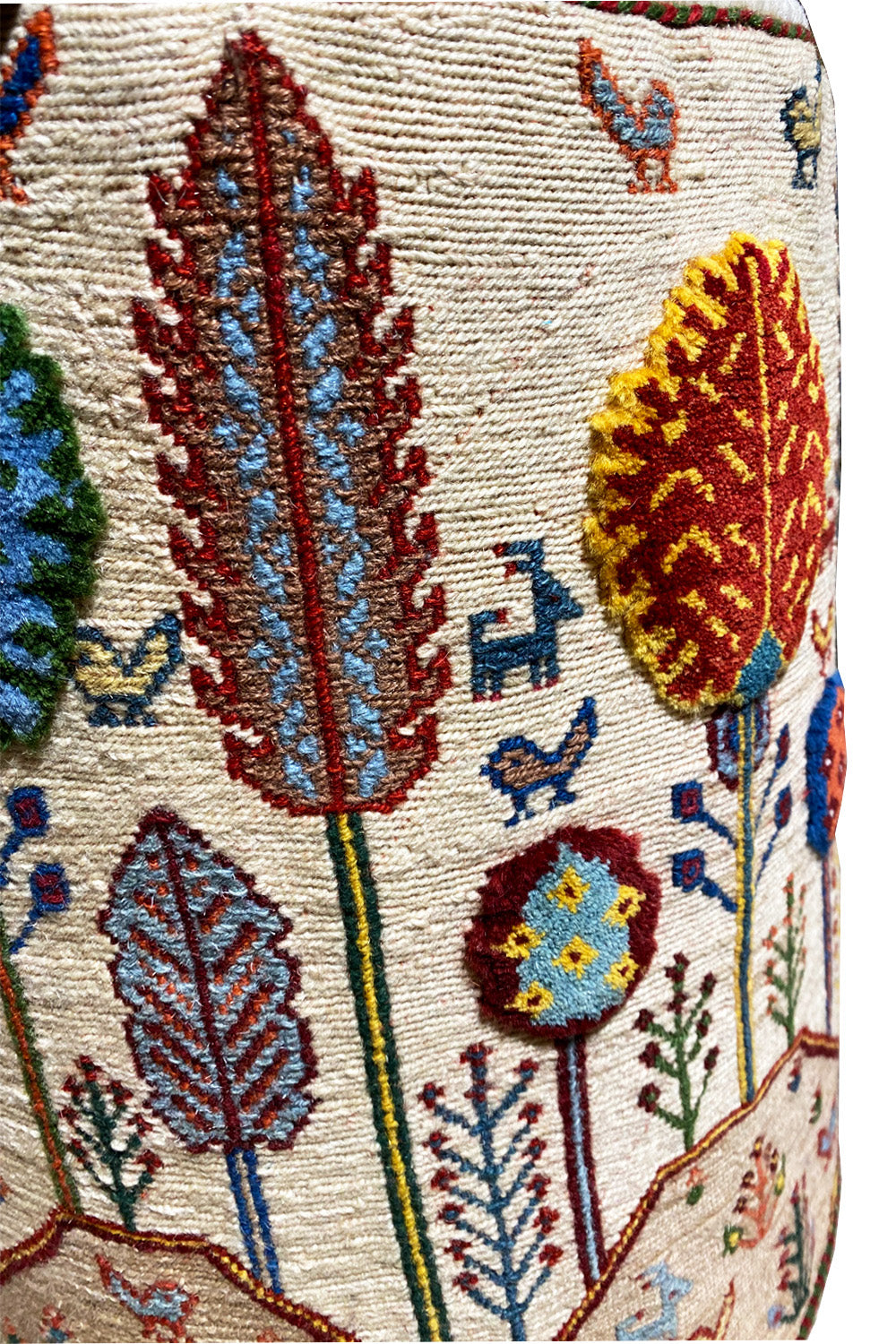 Close-up of the stool cover: embroidered leaves, blossoms, and small bird motifs on the fabric