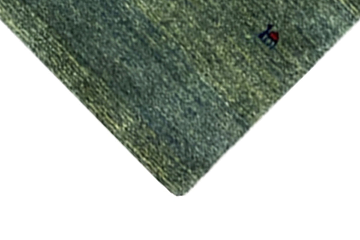 Corner of a Gabbeh rug with green pile and a blue-accented pattern detail
