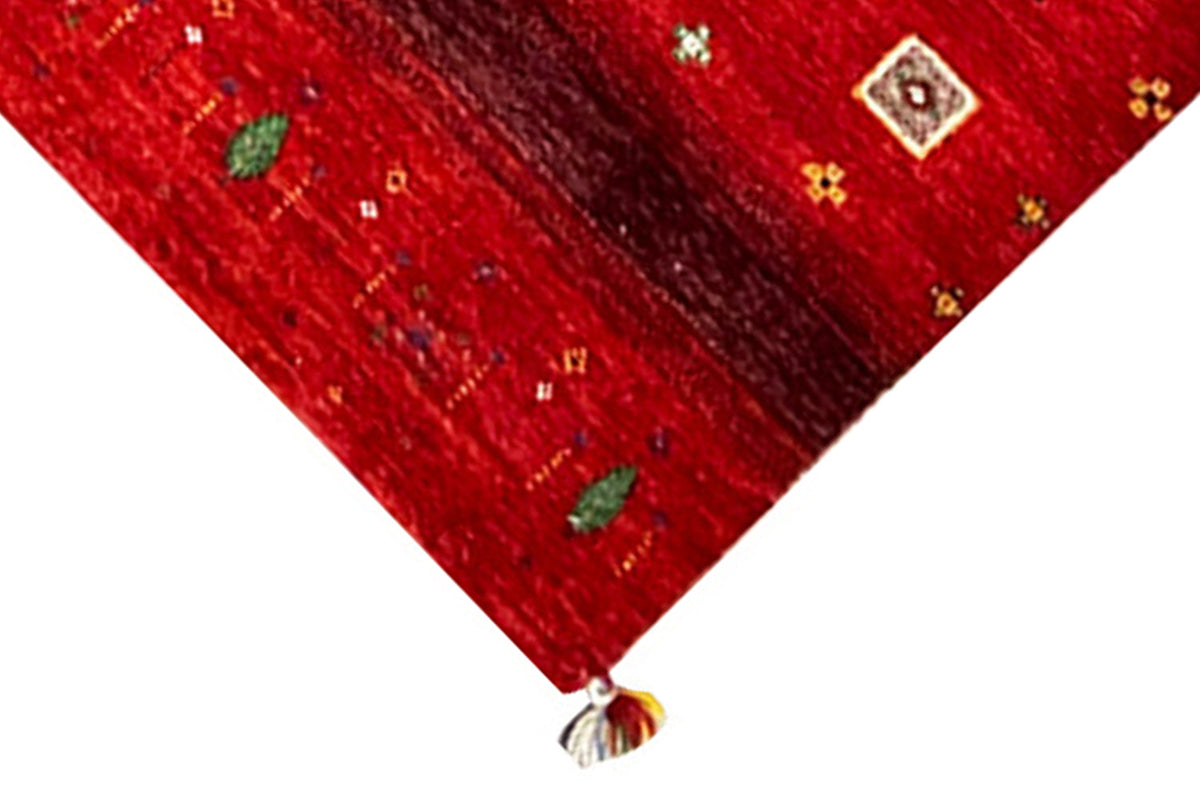 Corner of a red Gabbeh rug with a small pattern and fringe along the edge