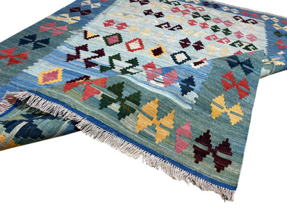 Blue kilim rug with a colorful pattern and fringes, diagonal view over the edge