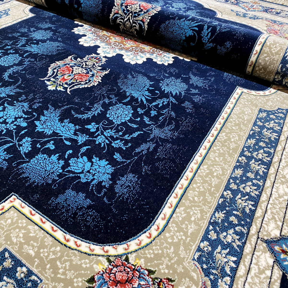 Close-up of a rolled Oriental rug: navy blue floral pattern, light border