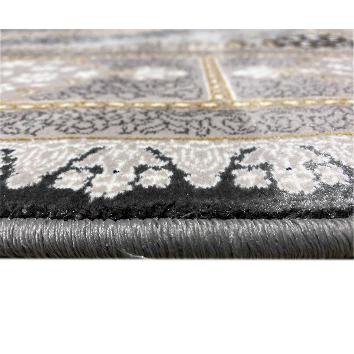 Close-up: rug edge with pile texture and fringe, patterned border in gray and gold