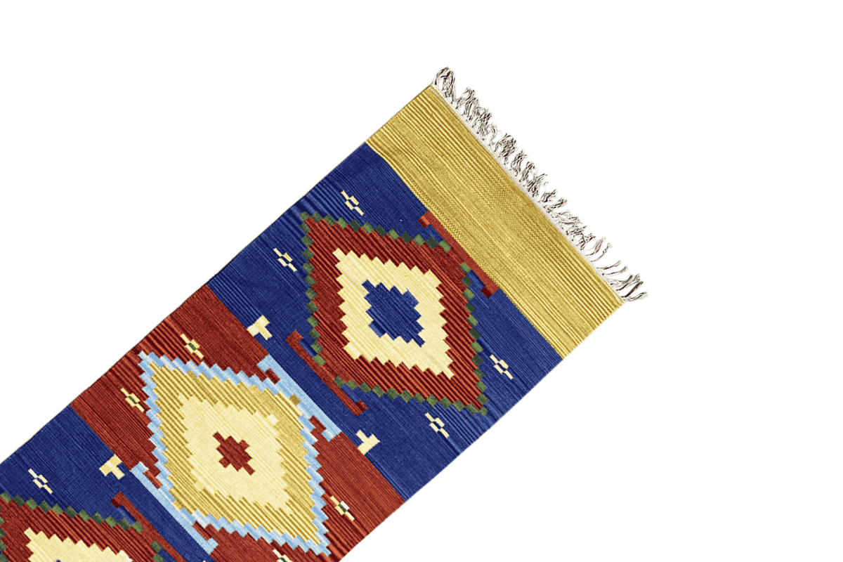 Corner detail of a wool kilim runner with a yellow border, blue and red diamonds, and fringes