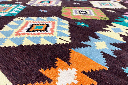 Close-up of a kilim rug: colorful squares and triangles on a dark textile surface