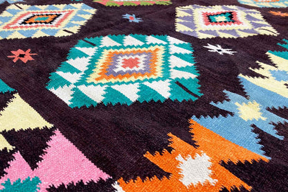 Close-up of a kilim rug: dark wool fabric with colorful squares and zigzag details