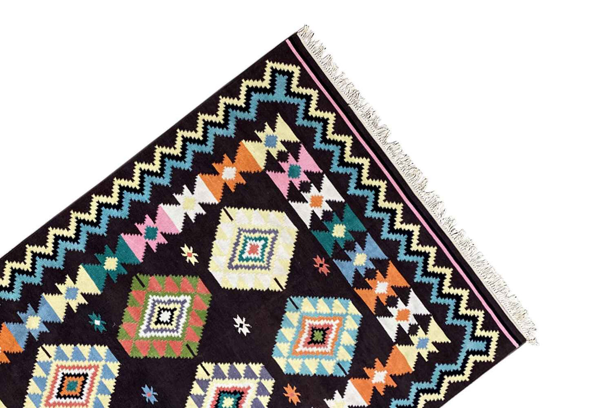 Corner view of a kilim rug with a framed zigzag pattern, colorful diamonds, and long fringes
