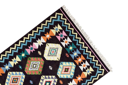 Corner view of a kilim rug with a framed zigzag pattern, colorful diamonds, and long fringes