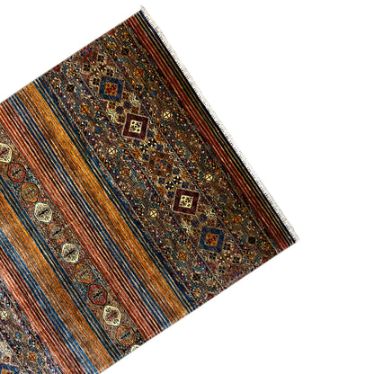 Colorful rug viewed at an angle, with a brown background, blue stripes, and embroidered decorative motifs.