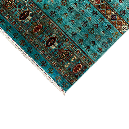 Corner of a turquoise rug with an ornamental border and white fringes