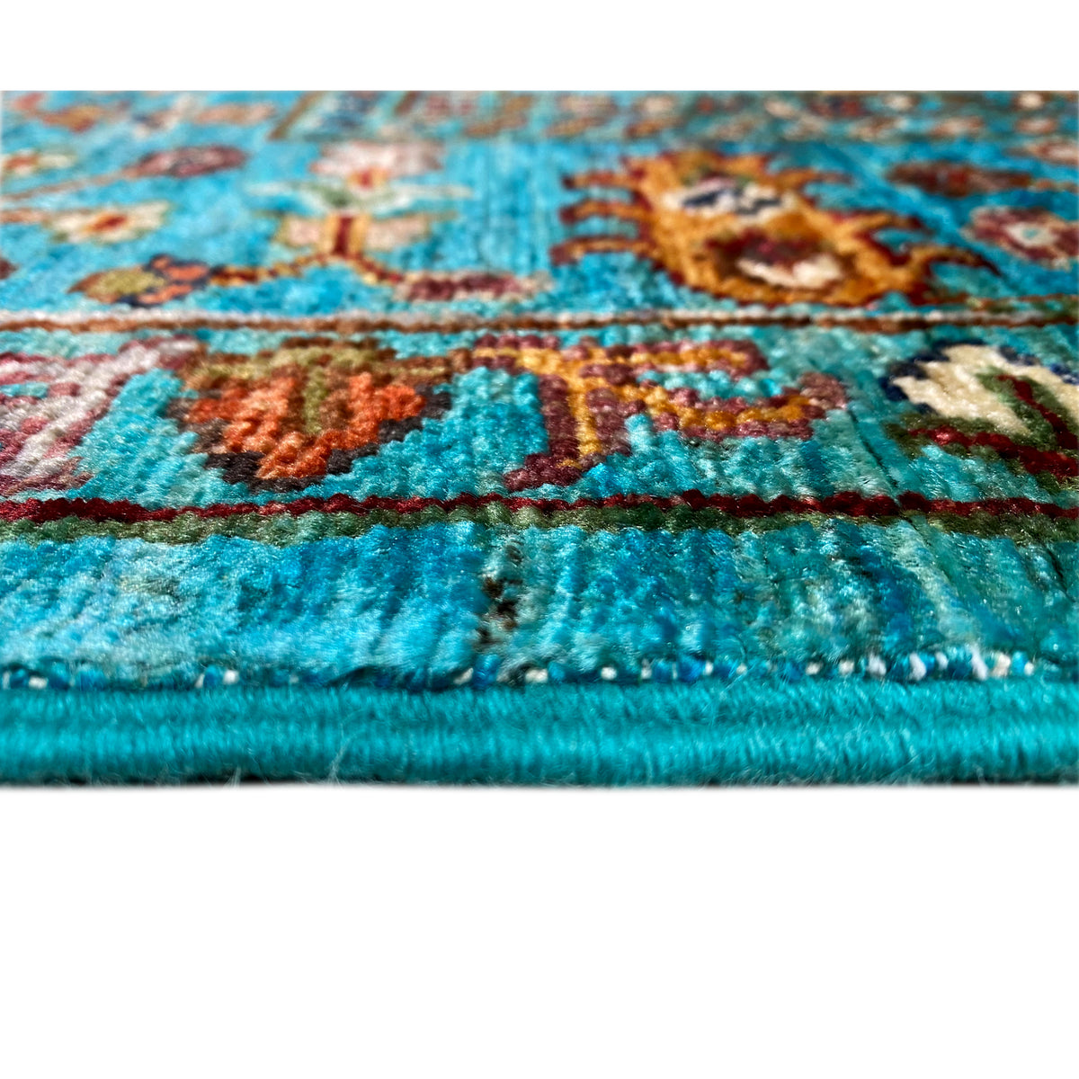 Side view of a turquoise Khorjin rug with floral motifs and fringes