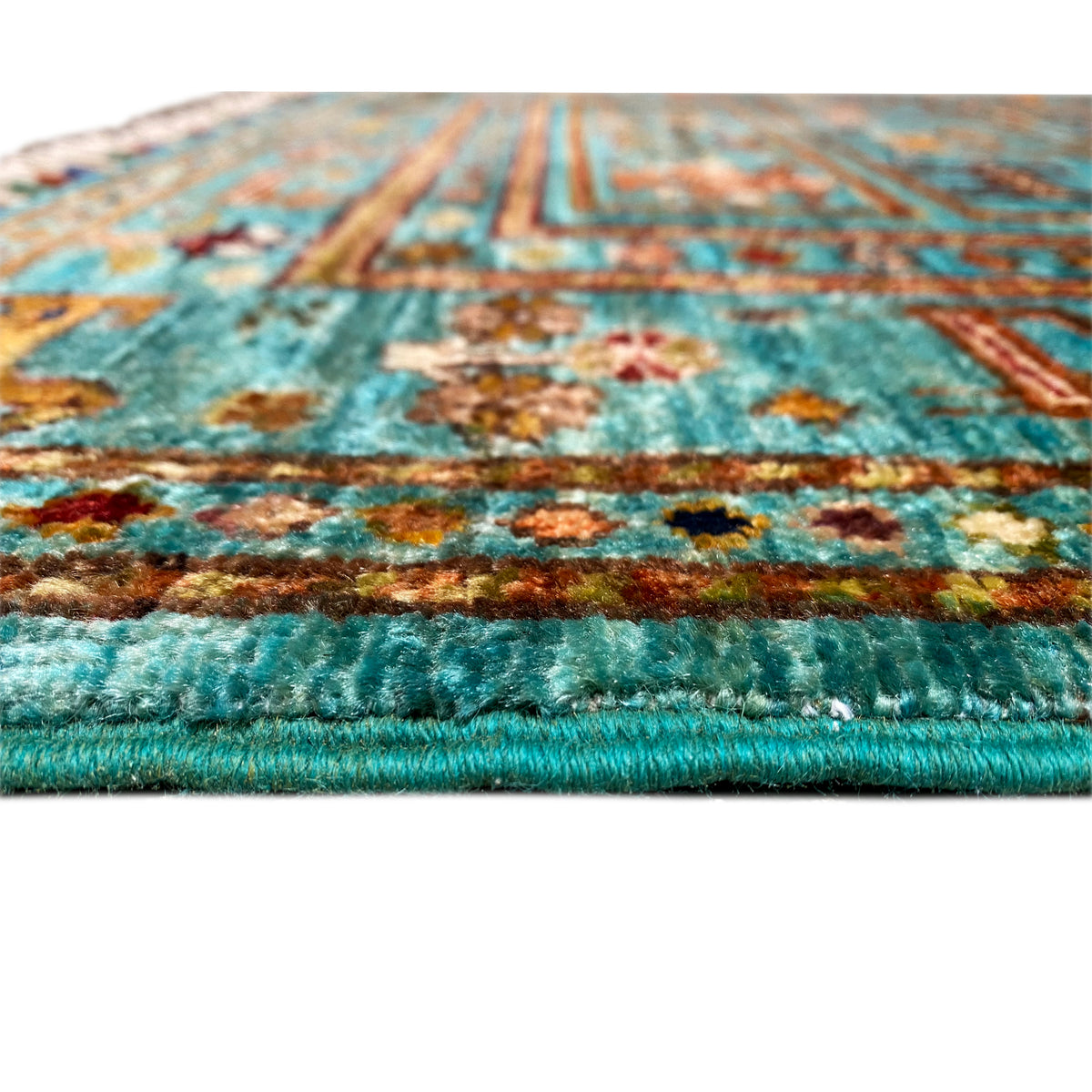 Close-up of a turquoise rug edge with floral motifs and a jagged fringed finish.