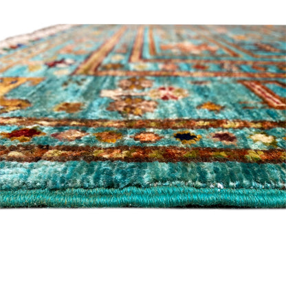 Close-up of a turquoise rug edge with floral motifs and a jagged fringed finish.