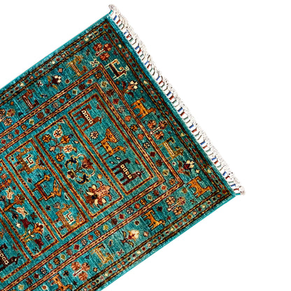 Corner of a turquoise Khorjin rug with ornaments and white fringe along the edge.