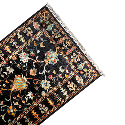 Khorjin rug 143x96 cm angled view: black background with colorful ornaments, fringed edge