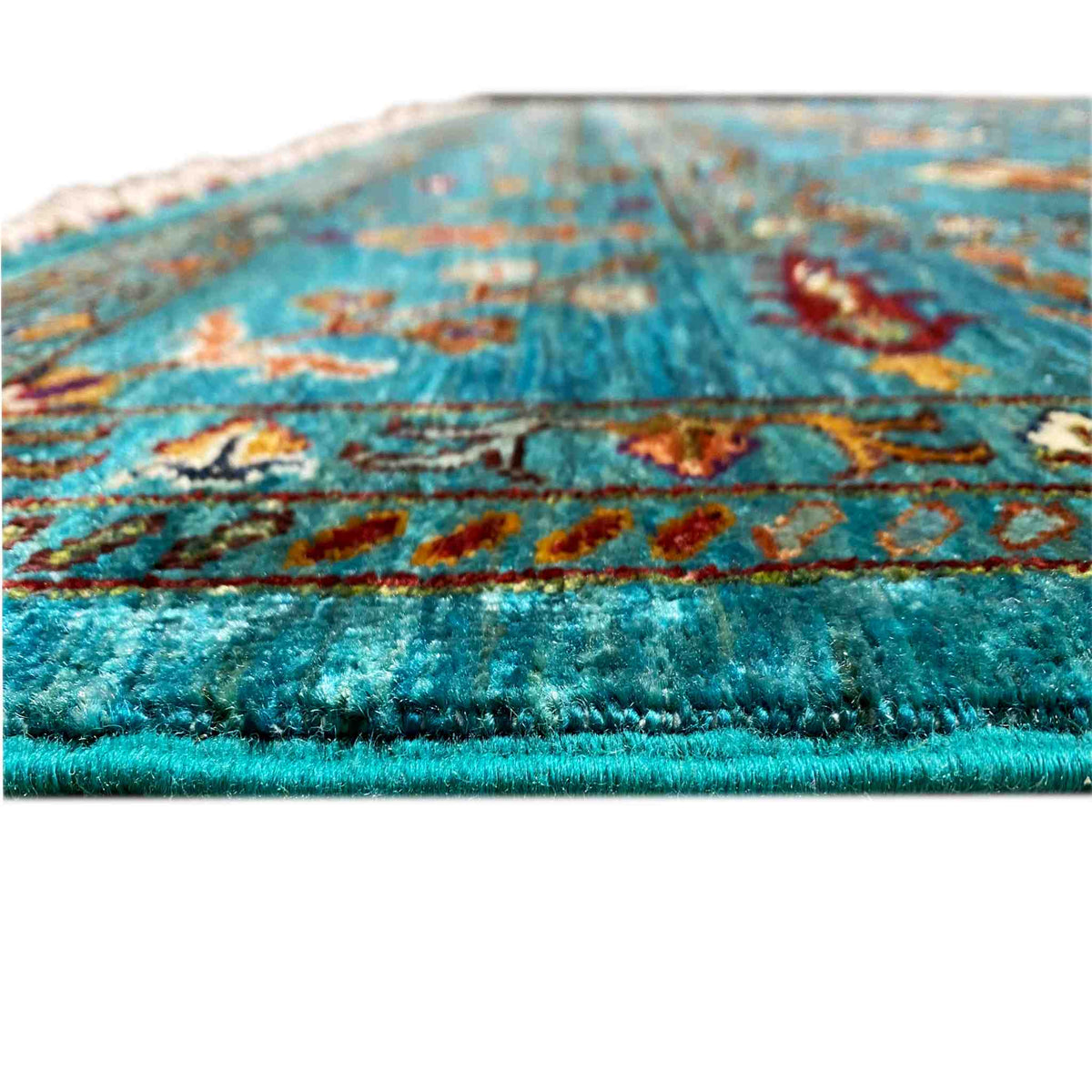 Close-up: turquoise carpet pile with colorful patterns, fringed edge