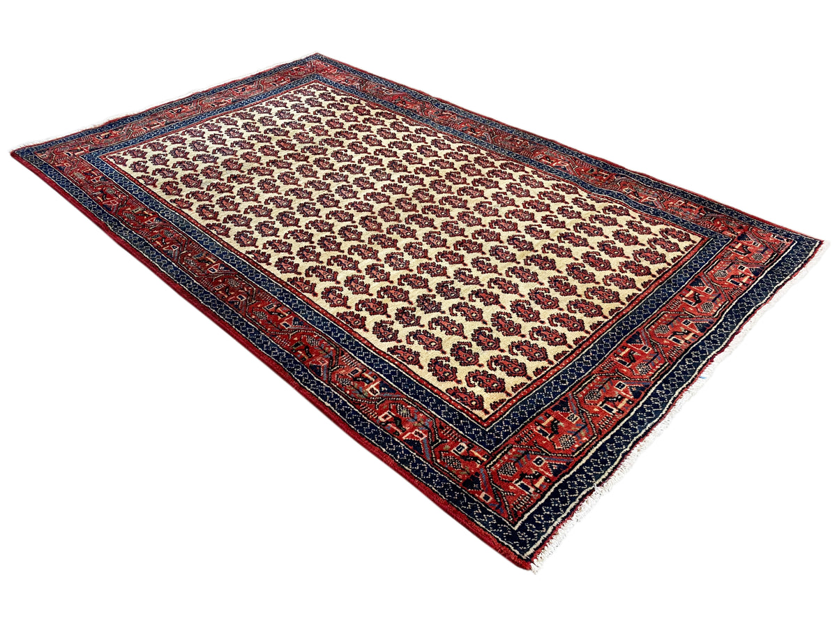 Oriental rug in cream with a red border and dark blue edging, diagonal view