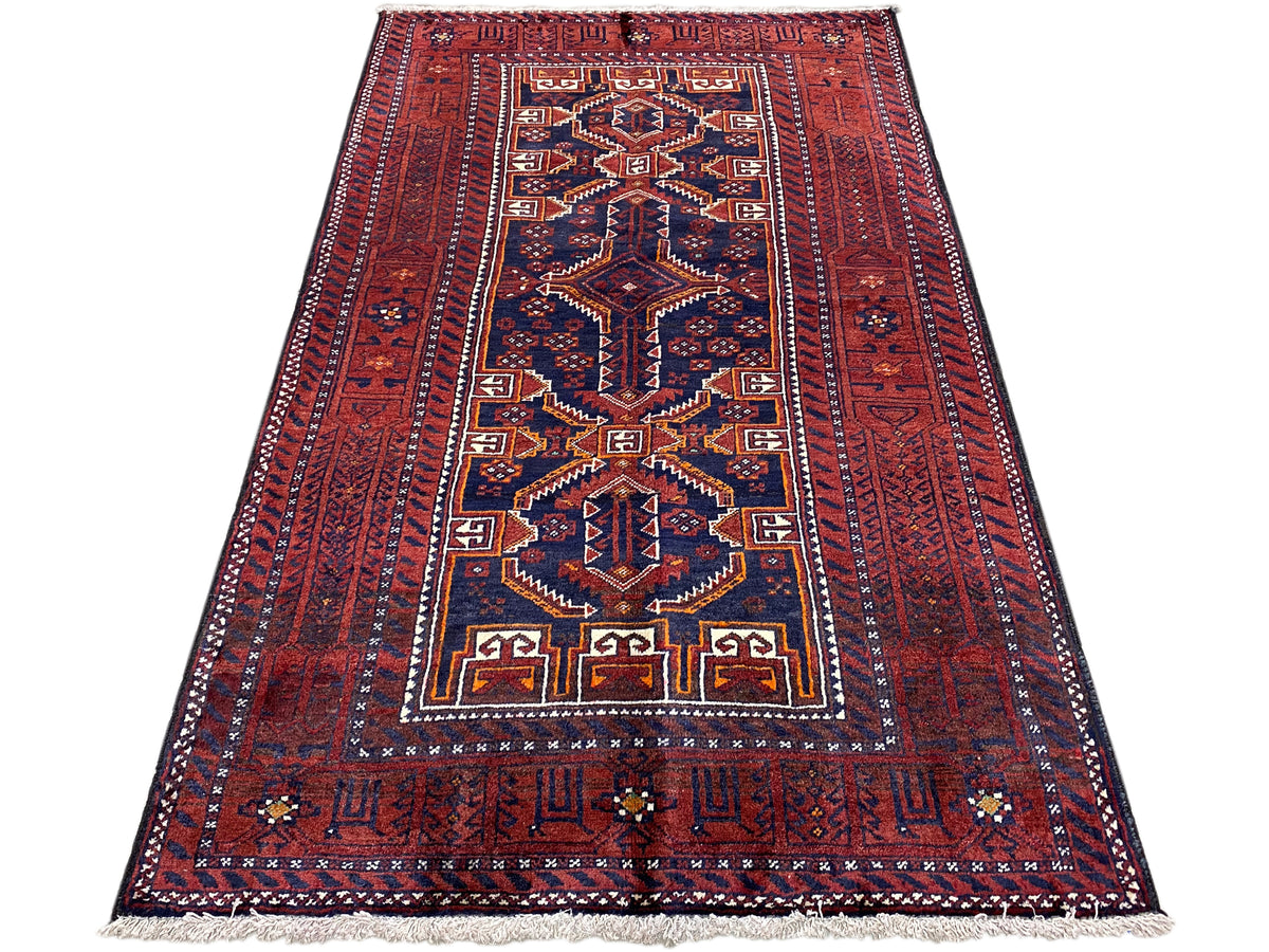 Rectangular Baluchi rug, red with blue and gold geometric designs, with fringes.
