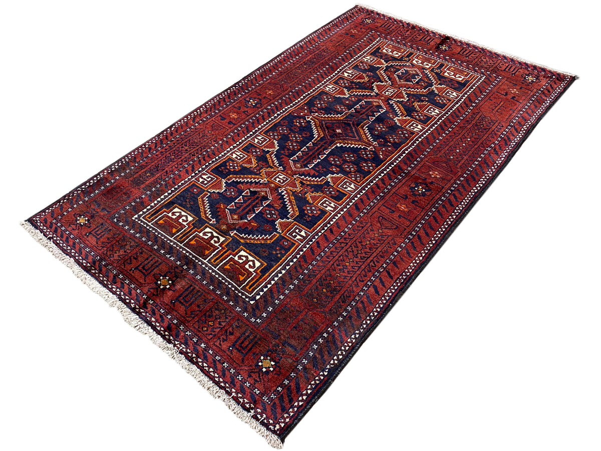 Rectangular Baluchi rug, red with a blue central motif, fine patterns, and fringes along the edges.